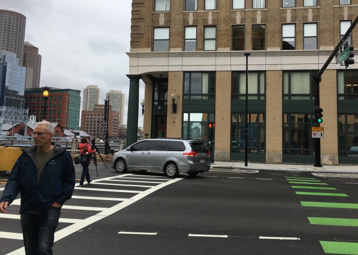 A motorist headed downtown from Melcher Street in the Fort Point neighborhood weaves around pedestrians on Sept. 12, 2019, in the same crosswalk where another motorist killed a pedestrian the night before. The City of Boston recently eliminated an exclusive pedestrian walk phase at this traffic signal.