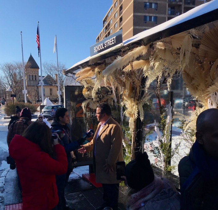 Everett Mayor Carlo DeMaria greets bus riders on Broadway in front of a bus shelter decked out in winter floral decorations on December 18. Courtesy of BostonBRT.