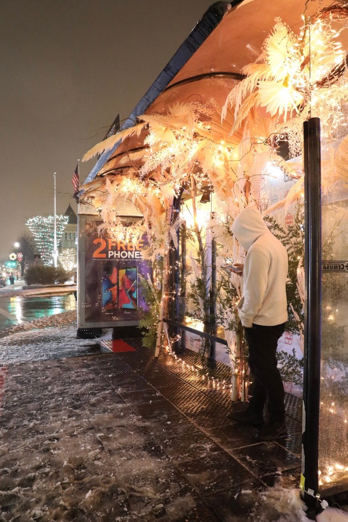 A bus stop in downtown Everett is decked out in flowers as snow falls on the evening of December 17, 2019. Photo courtesy of Boston BRT.