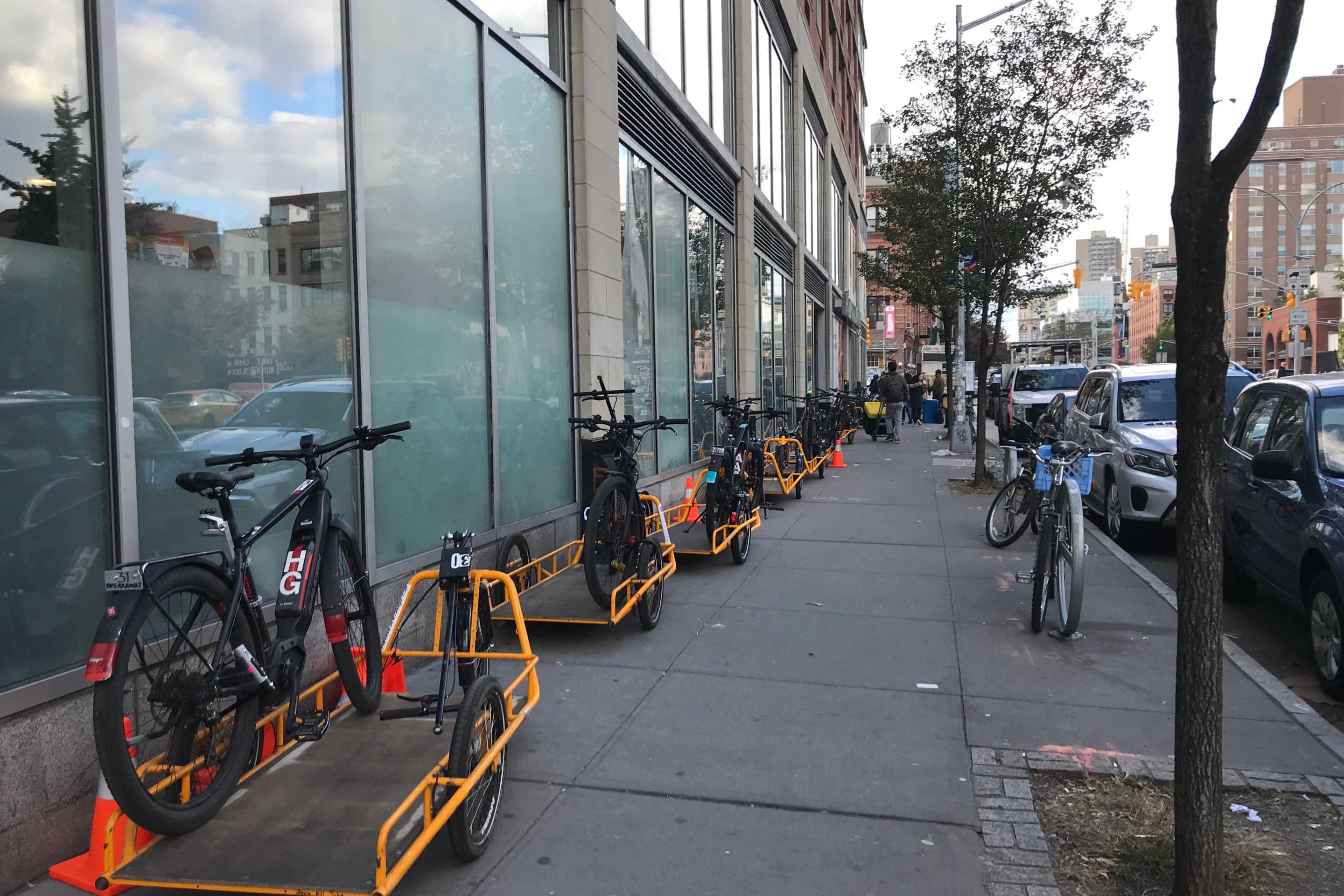 Cargo bikes and bike trailers parked on a sidewalk outside a Whole Foods Market in New York City