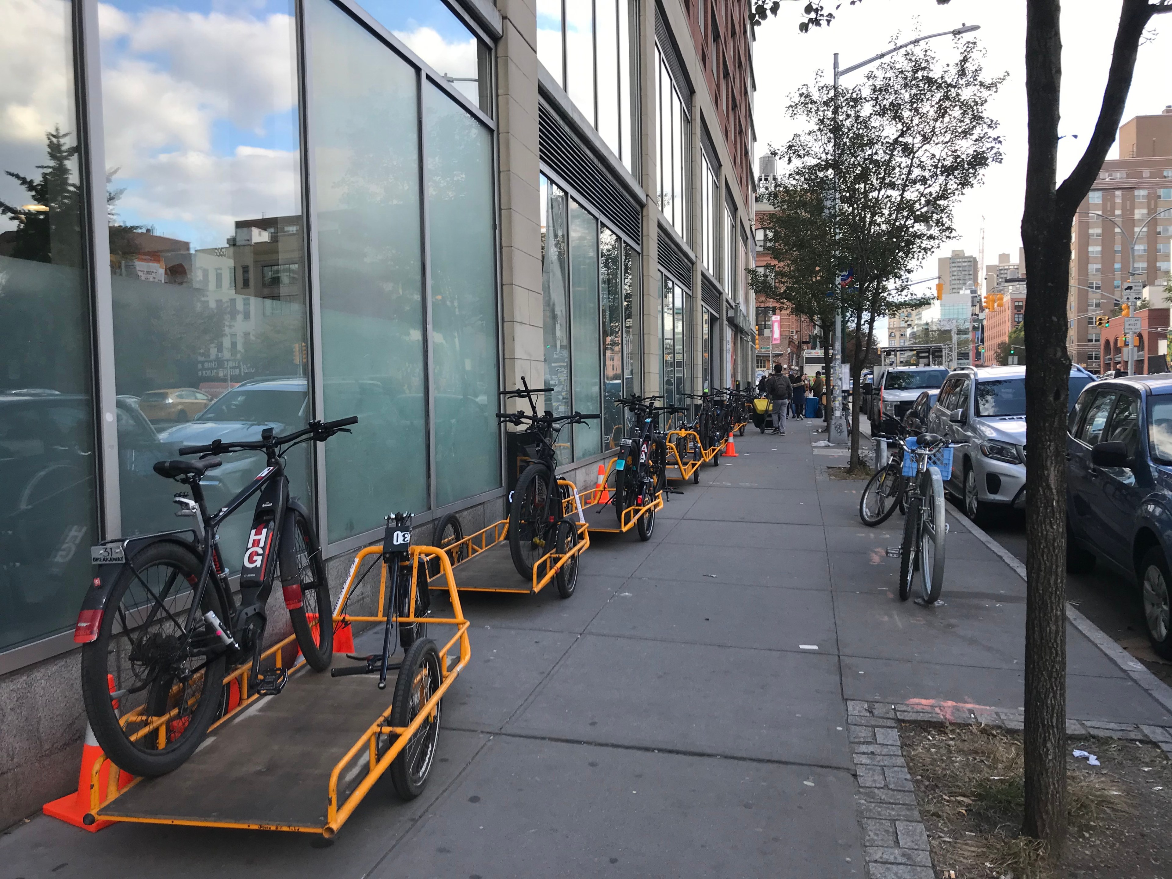 Cargo bikes and bike trailers parked on a sidewalk outside a Whole Foods Market in New York City