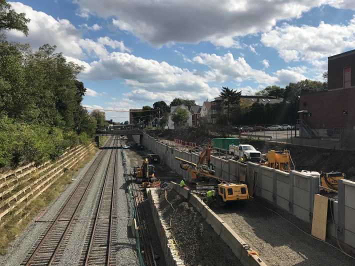 A view of the Green Line Extension under construction from the Central Street overpass. The new Community Path will cross Central Street above the Green Line here, and continue along the top of the retaining wall visible at right to cross both Sycamore Street and School Street, the two overpasses visible in the distance.