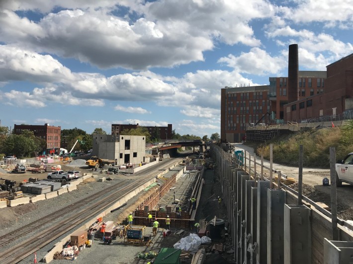 A view of the Gilman Square station under construction from the School Street overpass on Oct. 1, 2020. The concrete structure to the left of the tracks will be a power substation, and the Community Path will run along the embankment at the right of this photo.