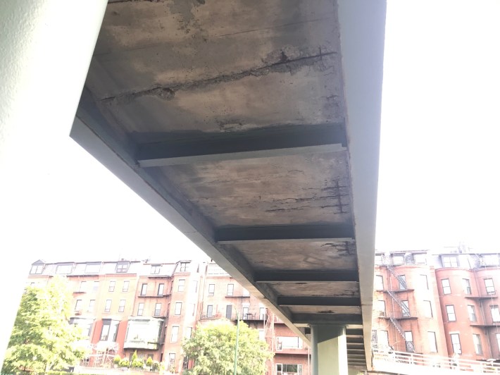 Underside of the Dartmouth Street pedestrian overpass over Storrow Drive, showing concrete failure and exposed, rusted rebar.