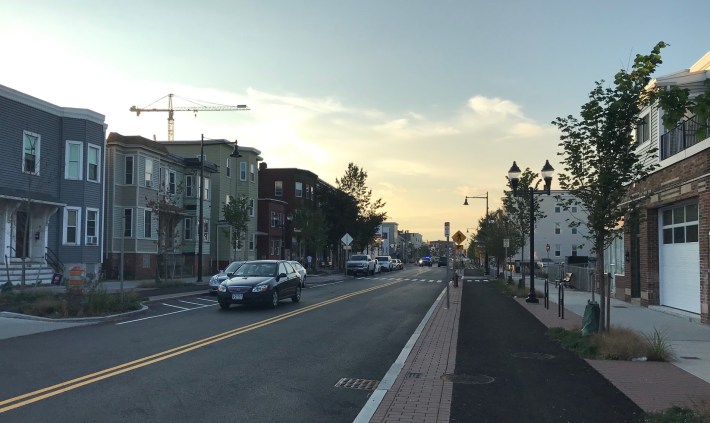 The newly reconstructed Somerville Ave., looking east toward Boston. The project installed sidewalk-level protected bike paths in each direction, new stormwater collection gardens, and improved sidewalks and crosswalks.
