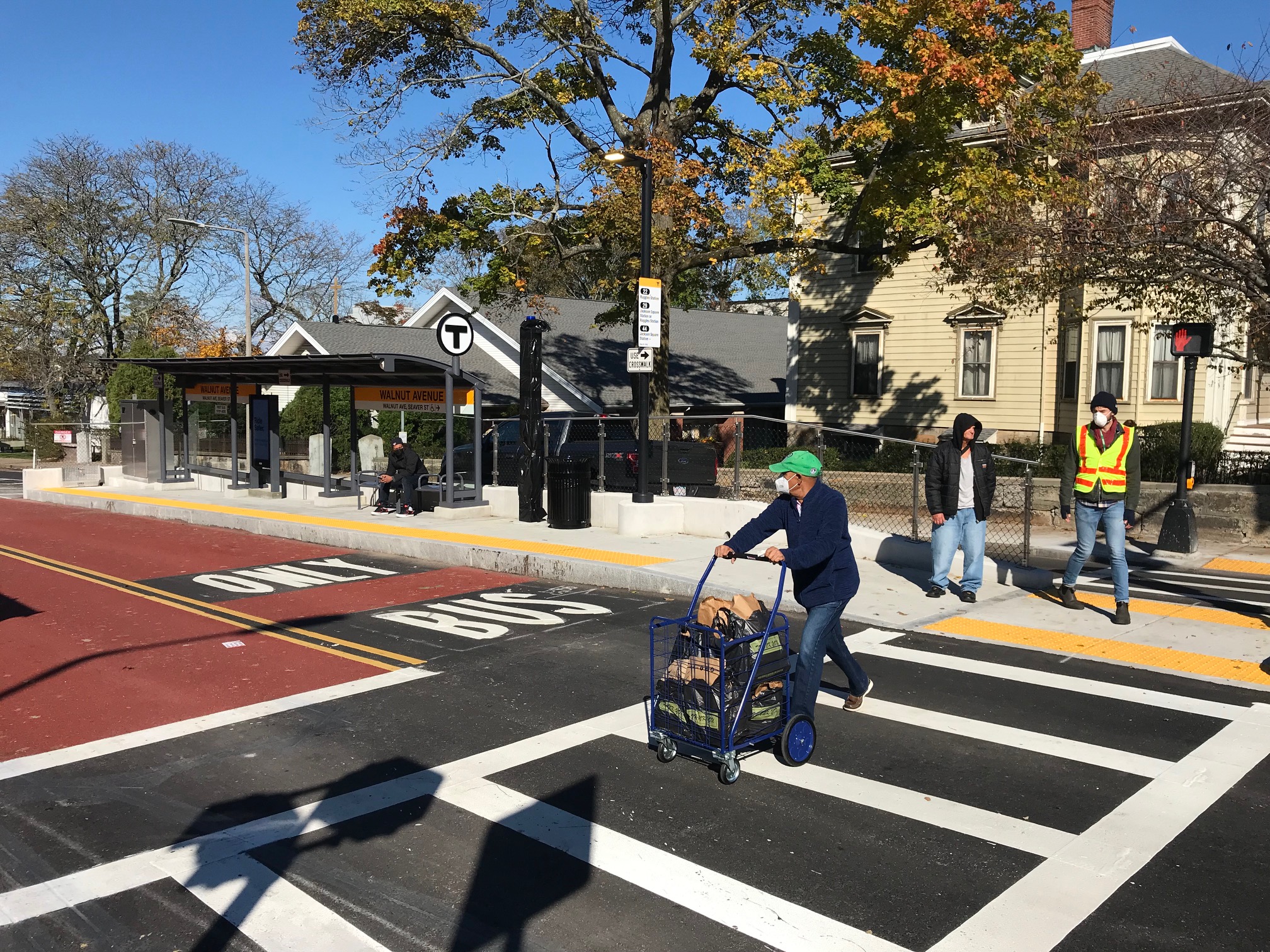 A photo of a pedestrian pushing a cart across the new crosswalk at the Walnut Ave. bus stop. The new bus platforms, in the middle of Columbus Avenue, essentially provide two safe refuges for people crossing the wide street.