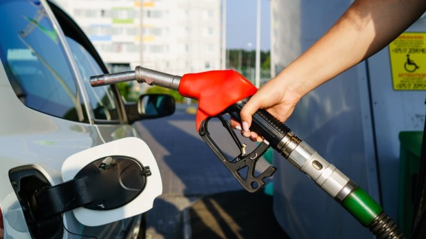 A hand holds a gasoline pump handle next to a car.