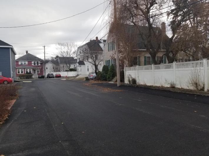 A photograph of Church Street in Natick after a recent repaving project. Both the sidewalks and the street were resurfaced in asphalt, making it extremely difficult to distinguish where the sidewalk is.