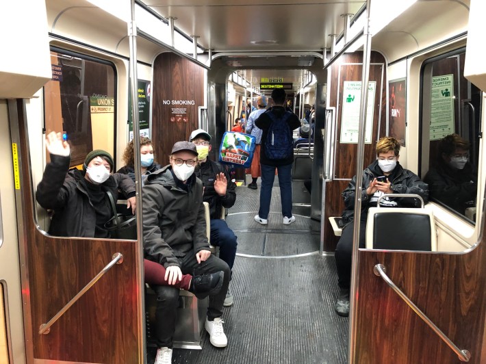 Masked riders wave and smile on the first Green Line train to depart from Somerville's new Union Square station.
