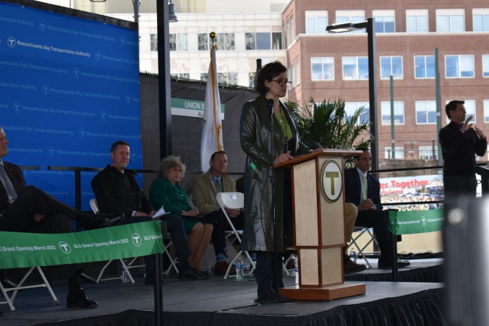 Somerville Mayor Katjana Ballantyne speaks from a podium at the Green Line Extension grand opening celebration, held in the plaza located under the new Lechmere Station in Cambridge