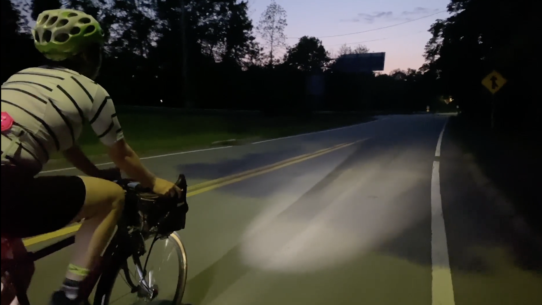 A woman bikes down a quiet suburban roadway at dusk.