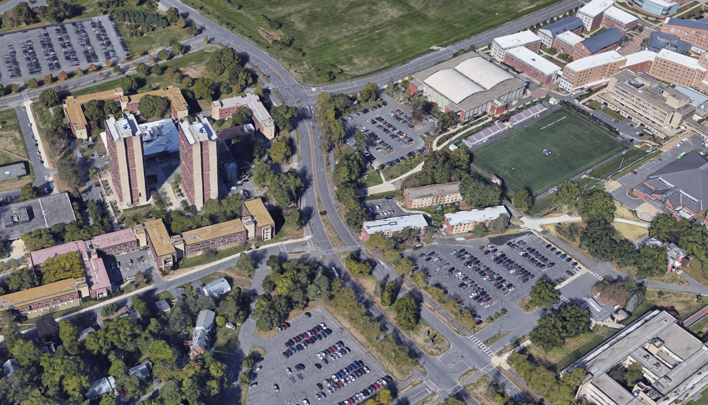 An aerial view of the UMass Amherst campus showing the 4-lane Massachusetts Avenue roadway dividing the residential dormitories (south of the road) from the campus's academic buildings (to the north).