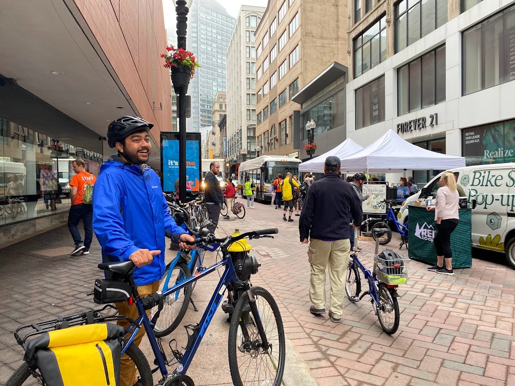 Person in blue jacket standing next to his bike by a crowd of other bikers in downtown Boston for Bike to Work Day festivities.