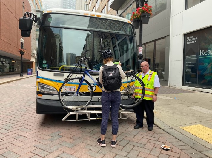 MBTA staff showing someone how to load their bike onto the front of a bus