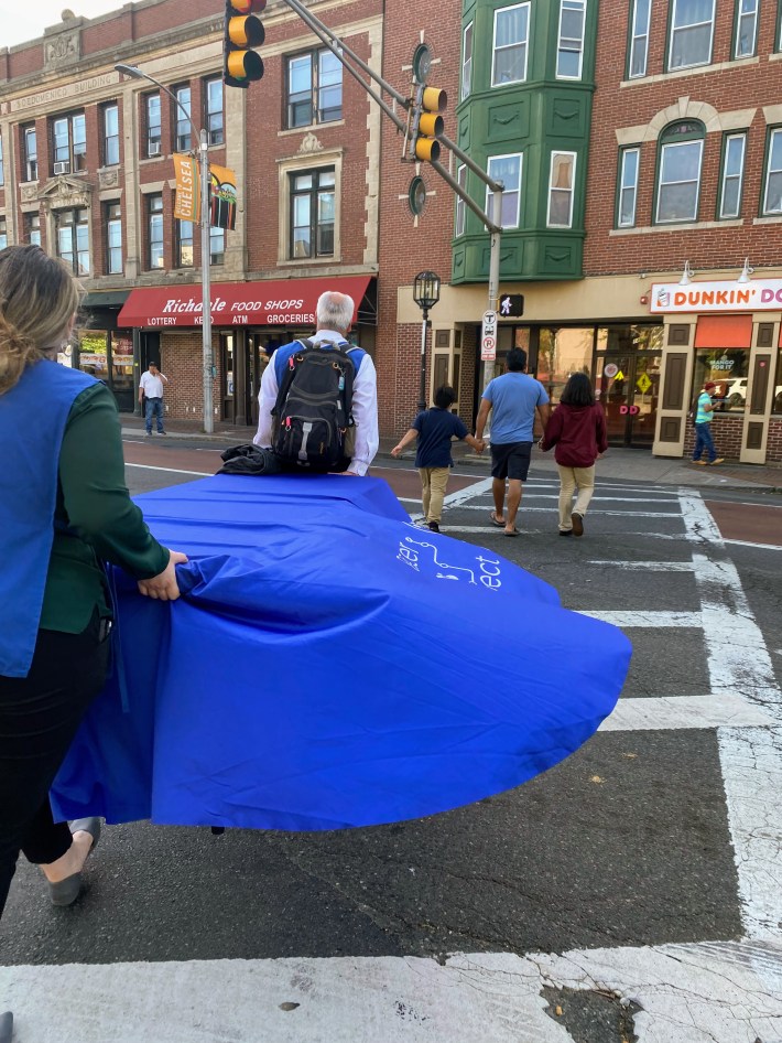 MBTA staff carry their table and supplies across to street to be closer to riders at a busy bus stop in downtown Chelsea.