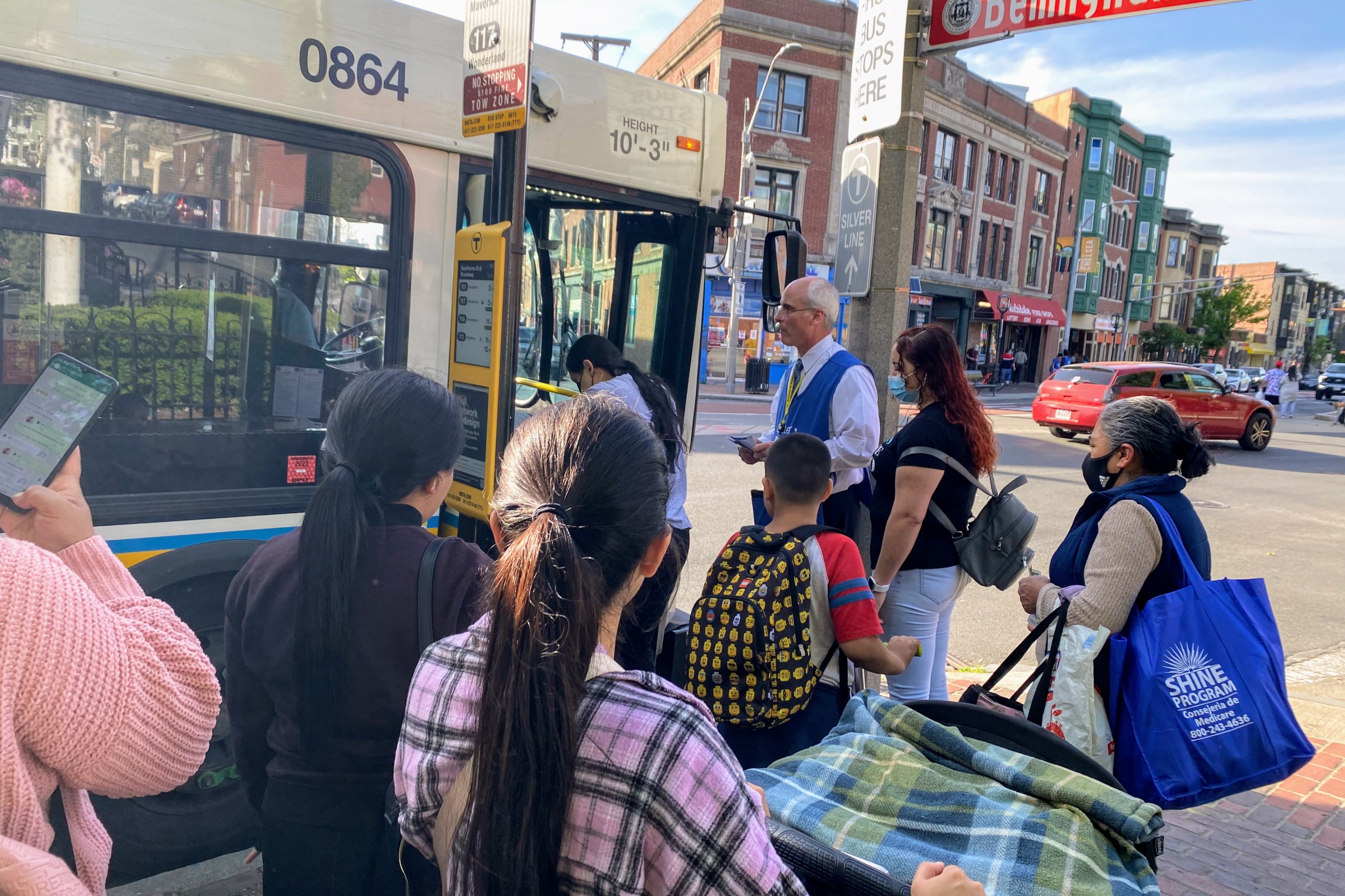 Pasajeros en Chelsea y un trabajador de alcance comunitario de la MBTA esperan abordar un autobús. Personal de la T compartieron información sobre el proyecto de Rediseño de la Red de Autobuses con pasajeros a bordo.