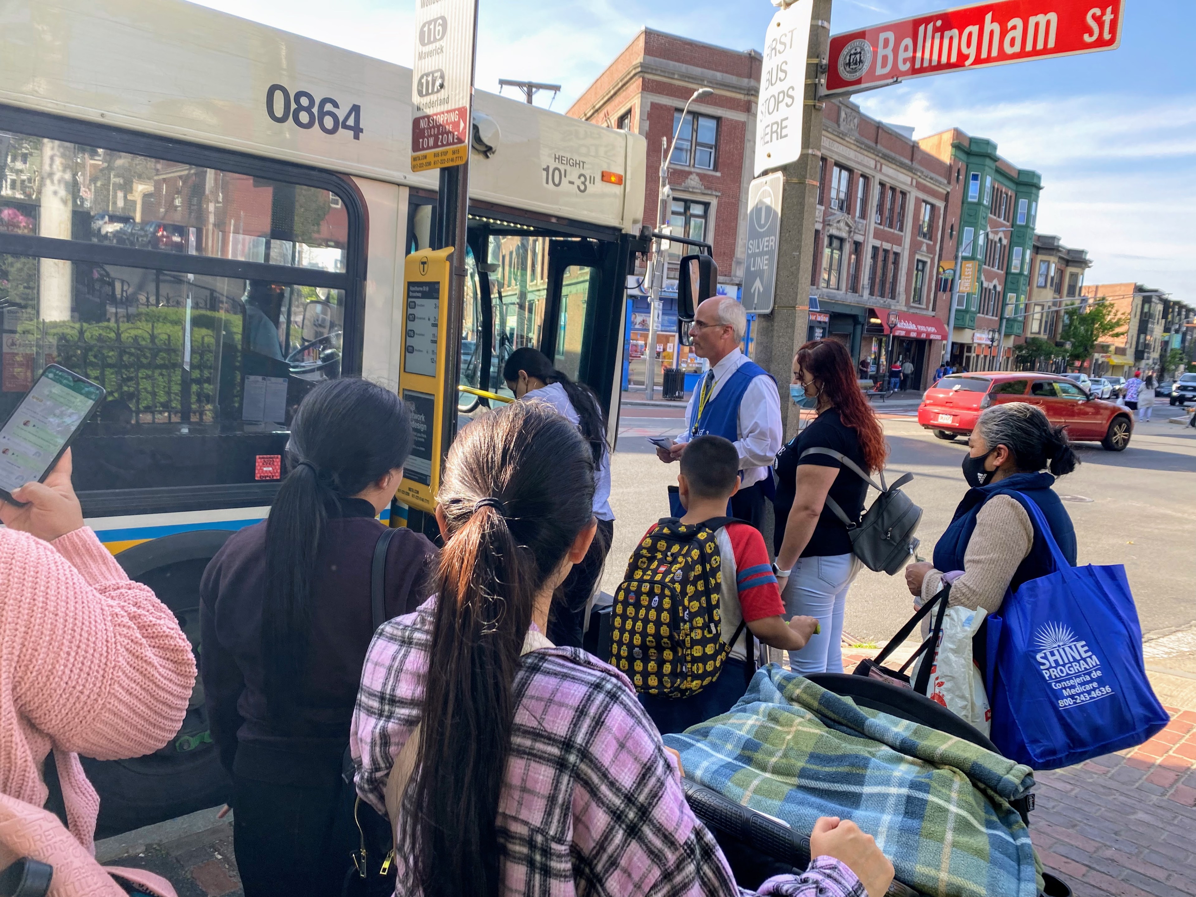 Pasajeros en Chelsea y un trabajador de alcance comunitario de la MBTA esperan abordar un autobús. Personal de la T compartieron información sobre el proyecto de Rediseño de la Red de Autobuses con pasajeros a bordo.