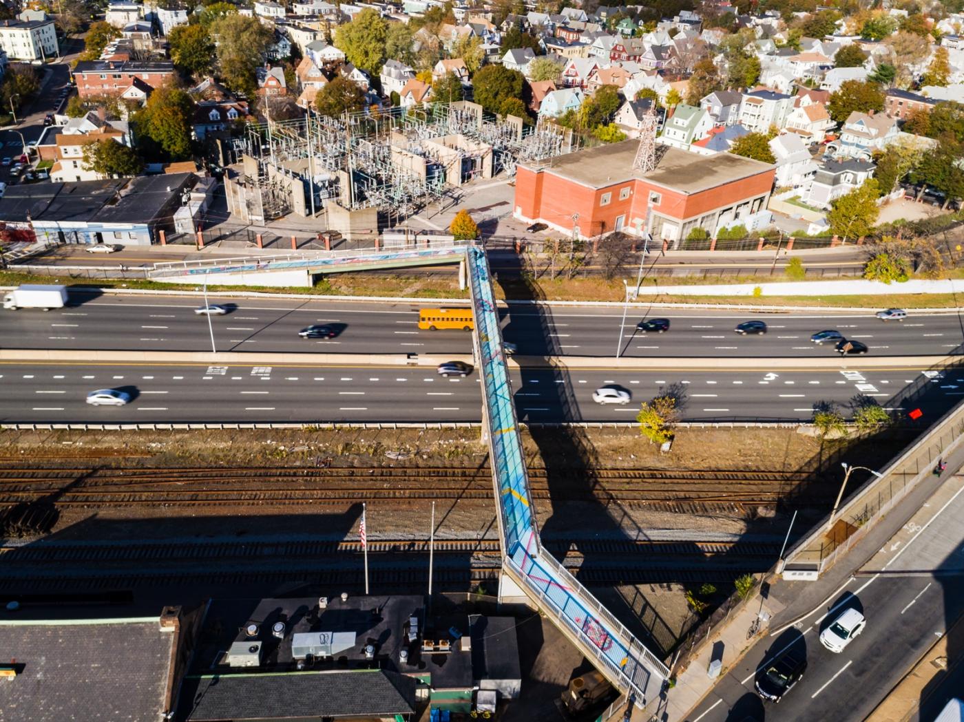An aerial photo of a brightly-colored footbridge across an eight-lane highway in Boston's Allston neighborhood.
