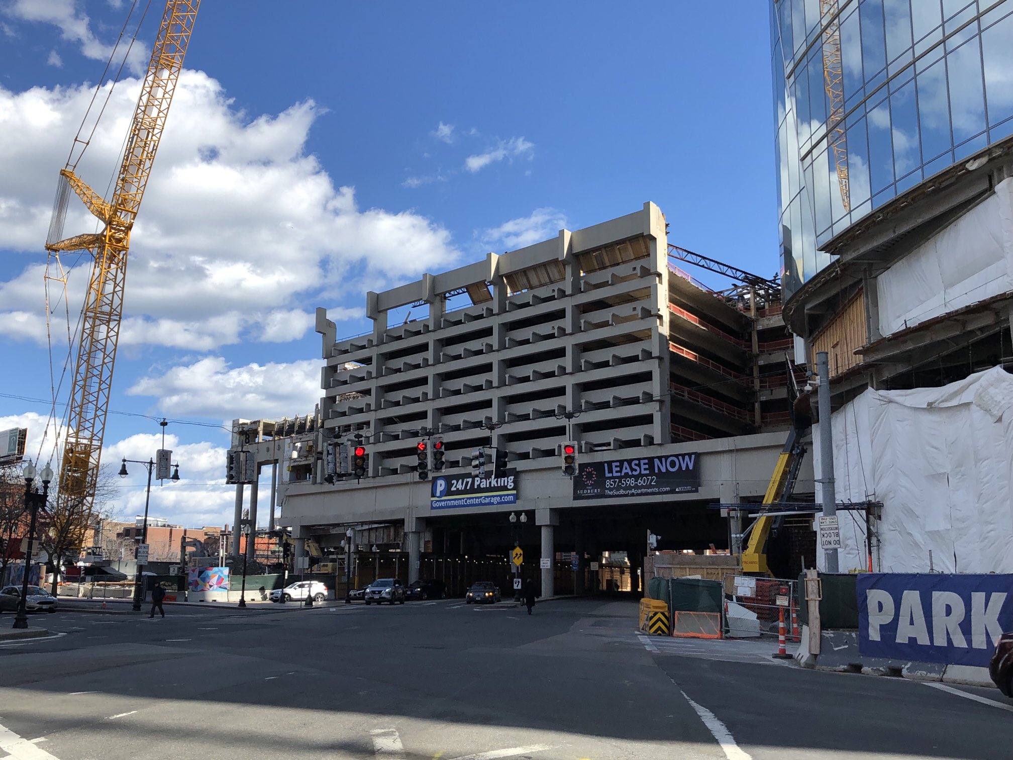 A large crane sits next to the Government Center parking garage in downtown Boston during its demolition. The left part of the garage is in the process of being taken apart, while the center portion that spans Merrimac Street (pictured in the foreground) is still intact