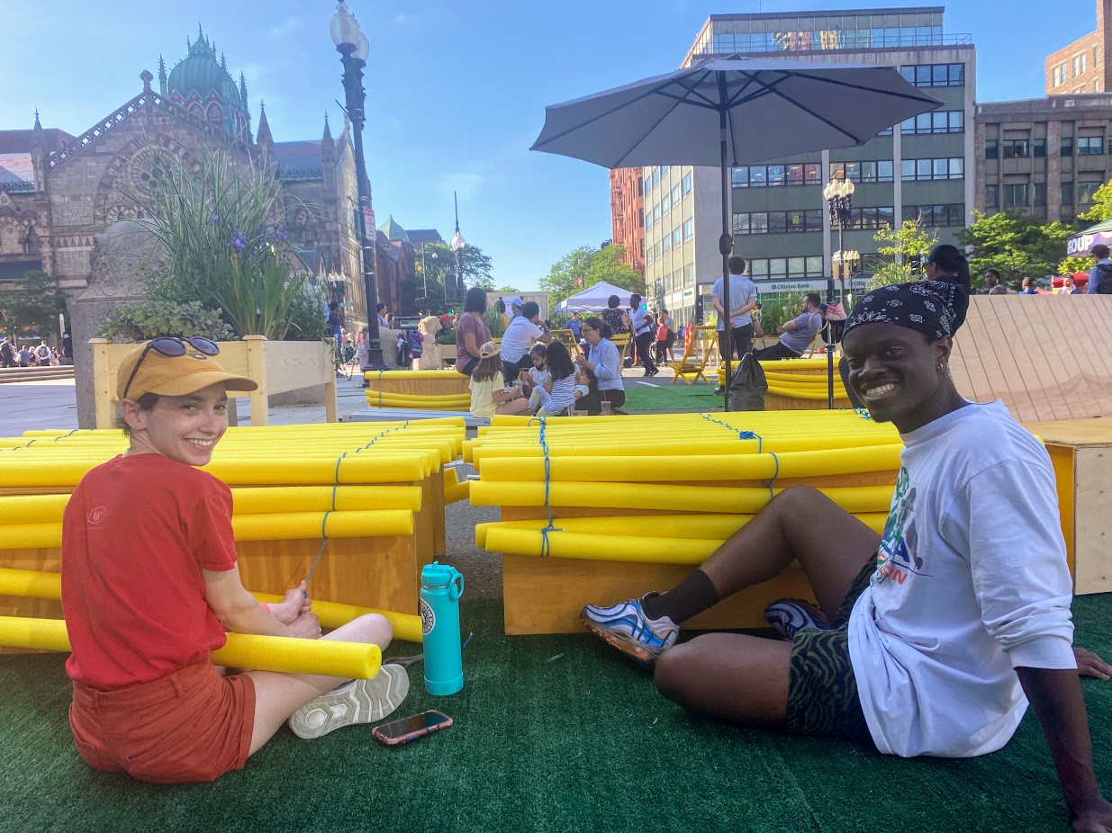 Two architecture students, Miranda and Denzel, string together pool noodles over wooden boxes - one of the many seating arrangements available for folks to enjoy in the city's "Copley Connect" pilot project
