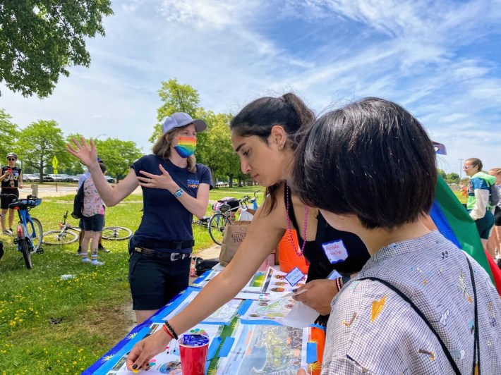 staff member wearing a tshirt and shorts explaining a project to ride participants