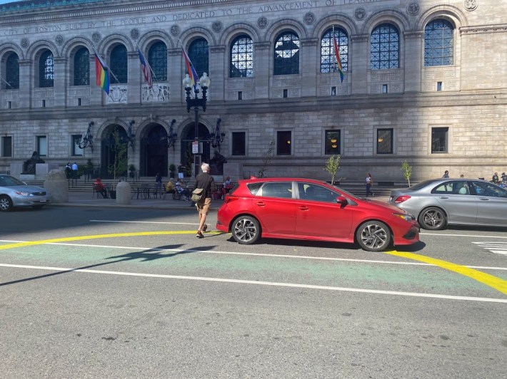 Person stepping into traffic to cross Dartmouth Street toward the Boston Public Library.