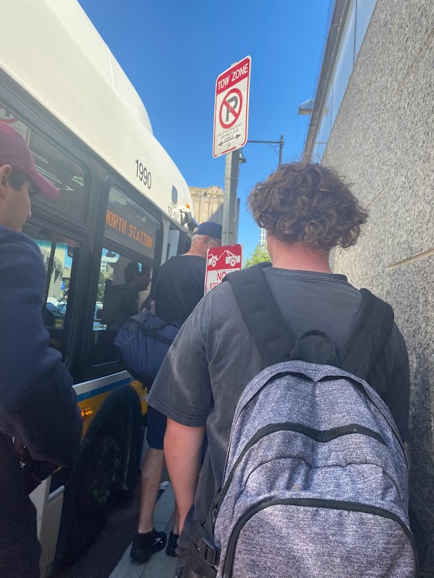 Crowds wait to board a shuttle bus from a crowded, narrow sidewalk near Government Center.