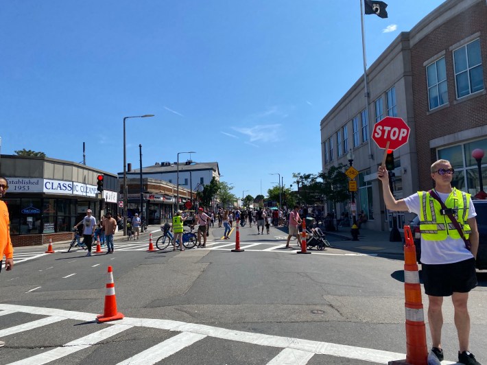 A man in a bright green vest holds up a stop sign while crowds of people on foot and on bikes wait to cross behind him.