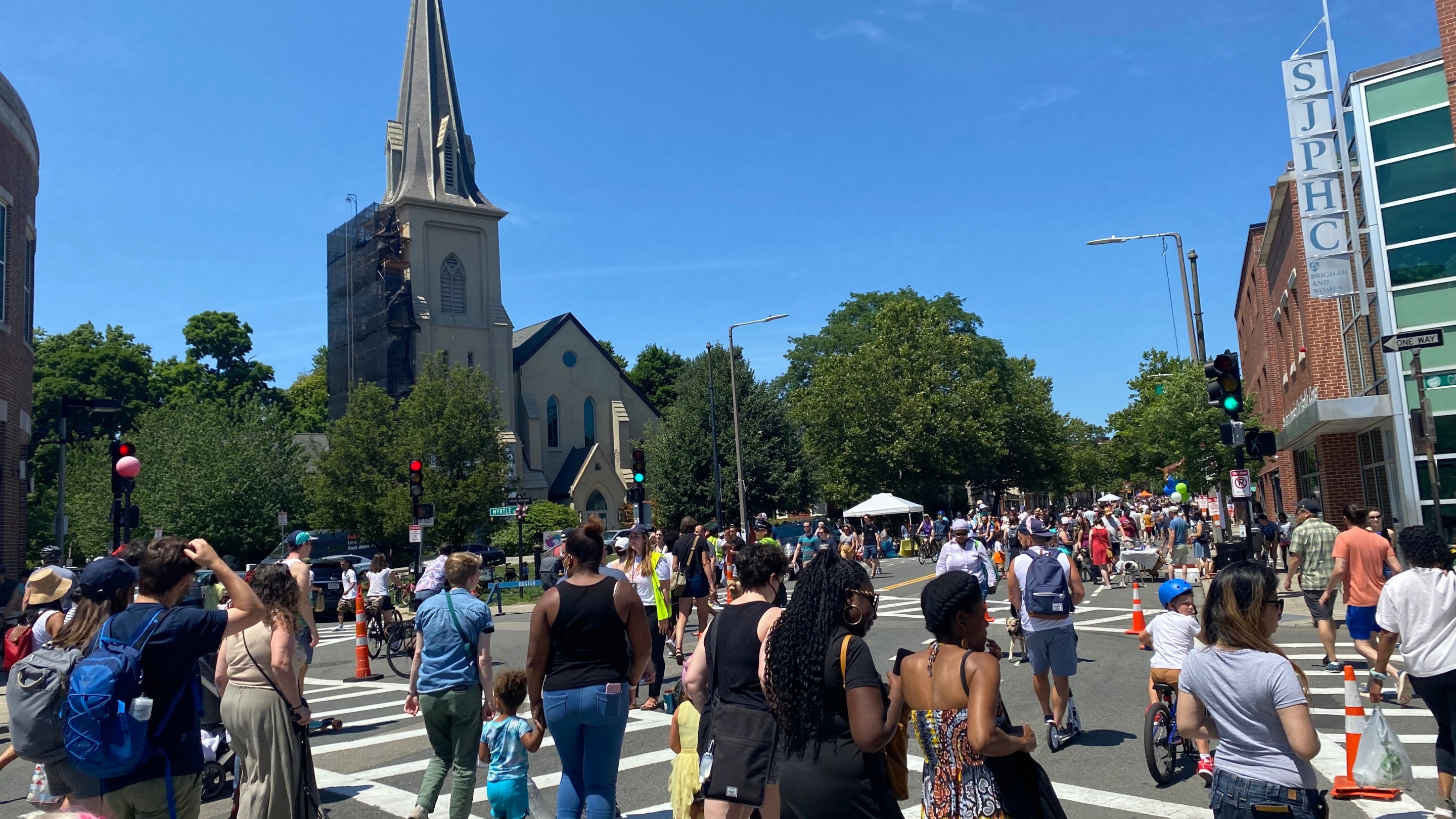 A large crowd of people walking and biking fills an intersection in front of a large church steeple.