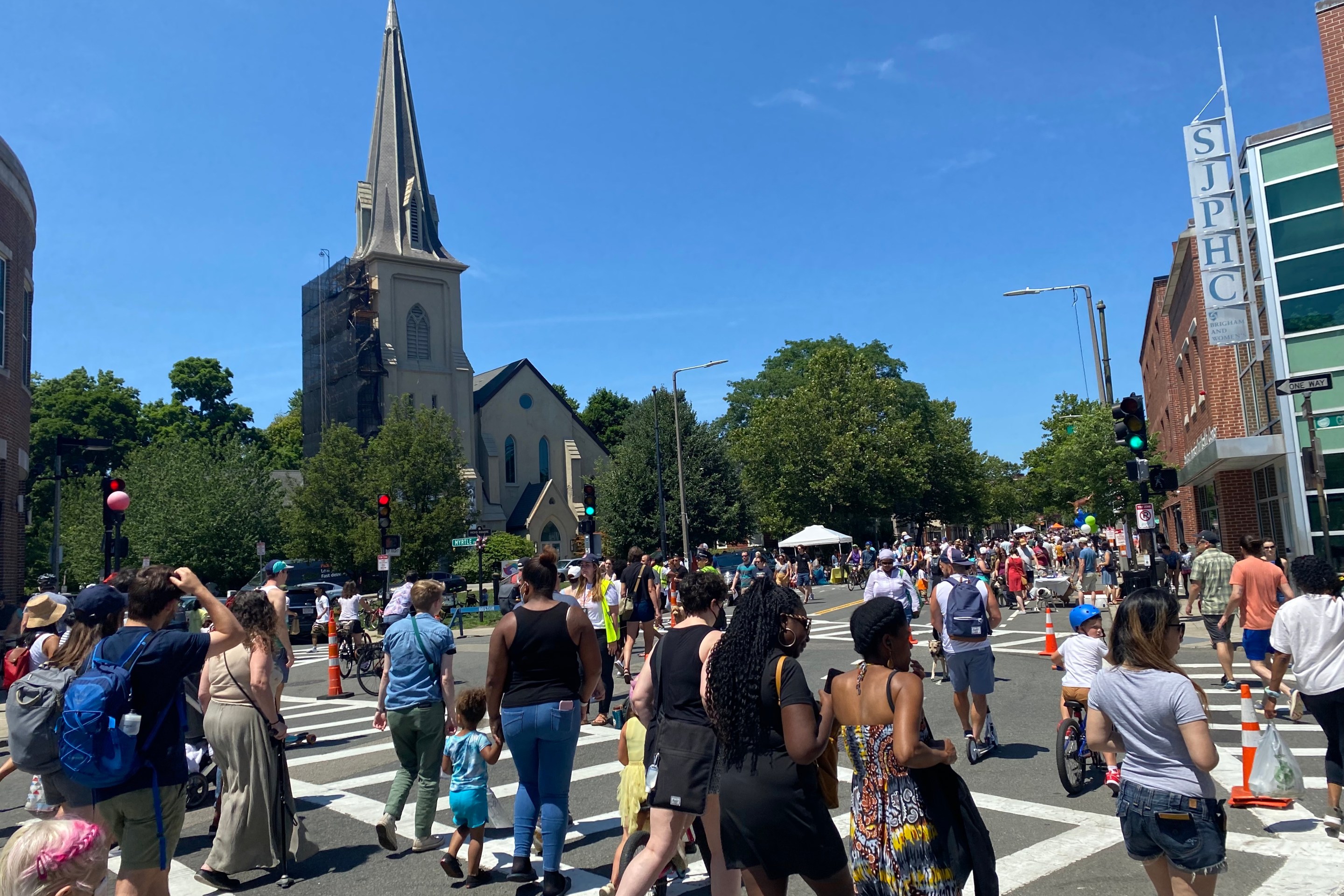 A large crowd of people walking and biking fills an intersection in front of a large church steeple.