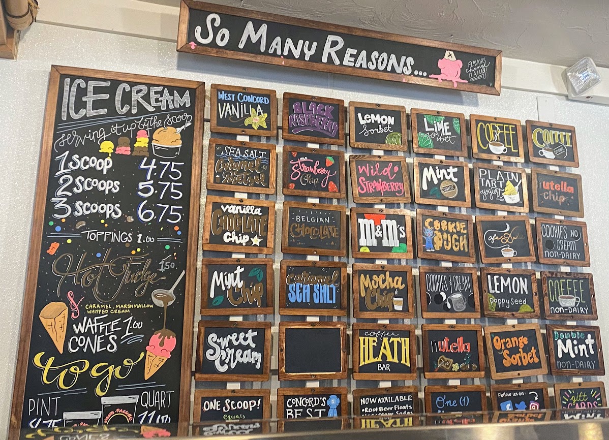 A wall covered in small chalkboards displaying roughly 60 ice cream flavors.