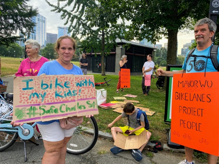 A family of three holds signs in Boston Common in support of better bike lanes on Charles Street.