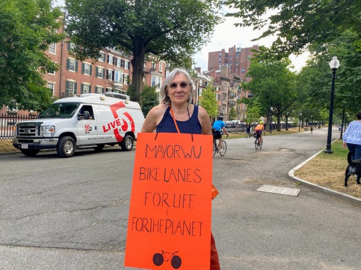 a woman holding a bright sign that says "Mayor Wu bike lanes for life for the planet"