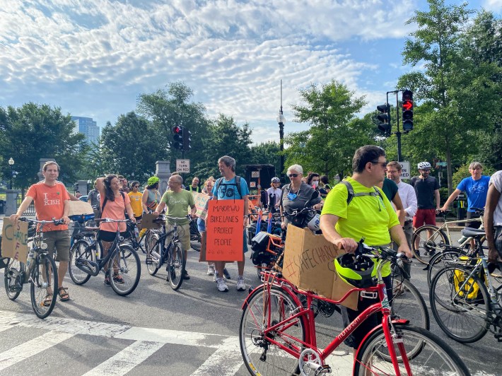 A crowd of people with bikes walks across the Beacon Street crosswalk.