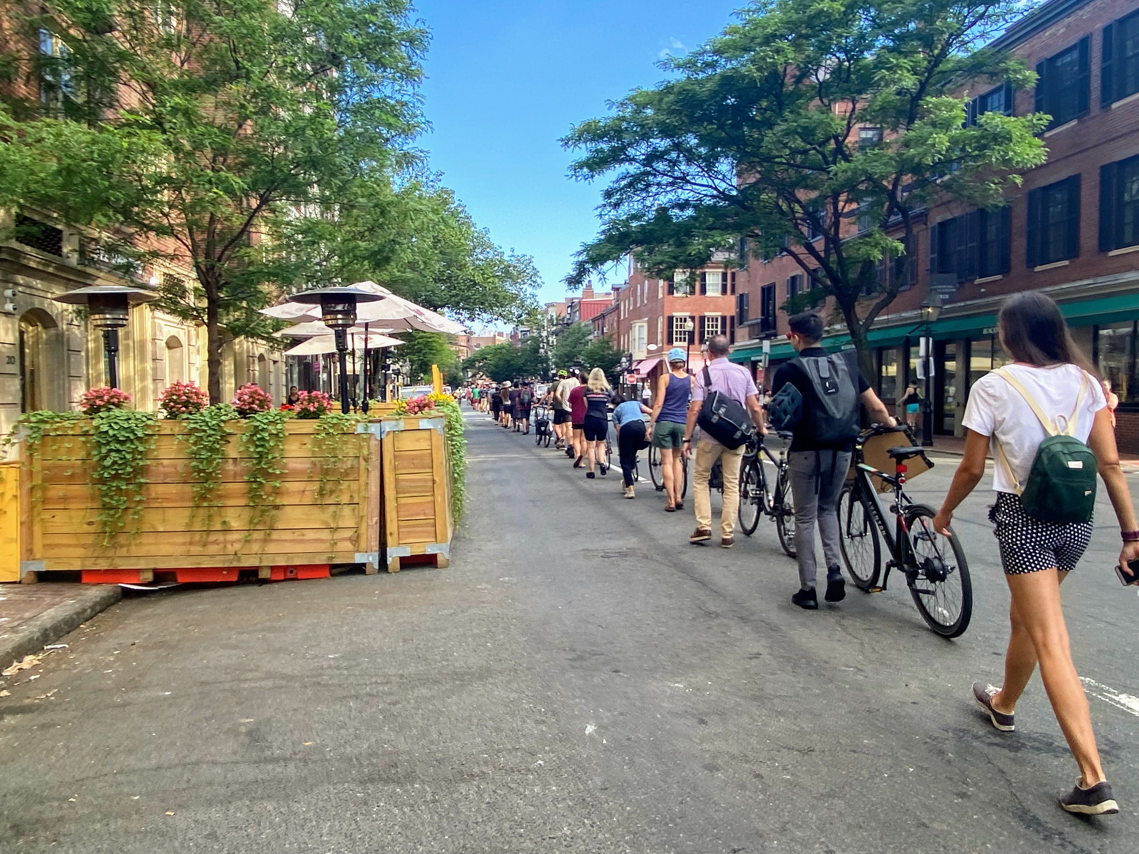 A chain of people, mostly with bikes, line up along the right lane of Charles Street in Beacon Hill to form a temporary "people-protected" bike lane.