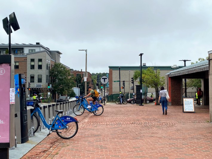 a bluebike station with few bikes left outside of a train station on a cloudy day