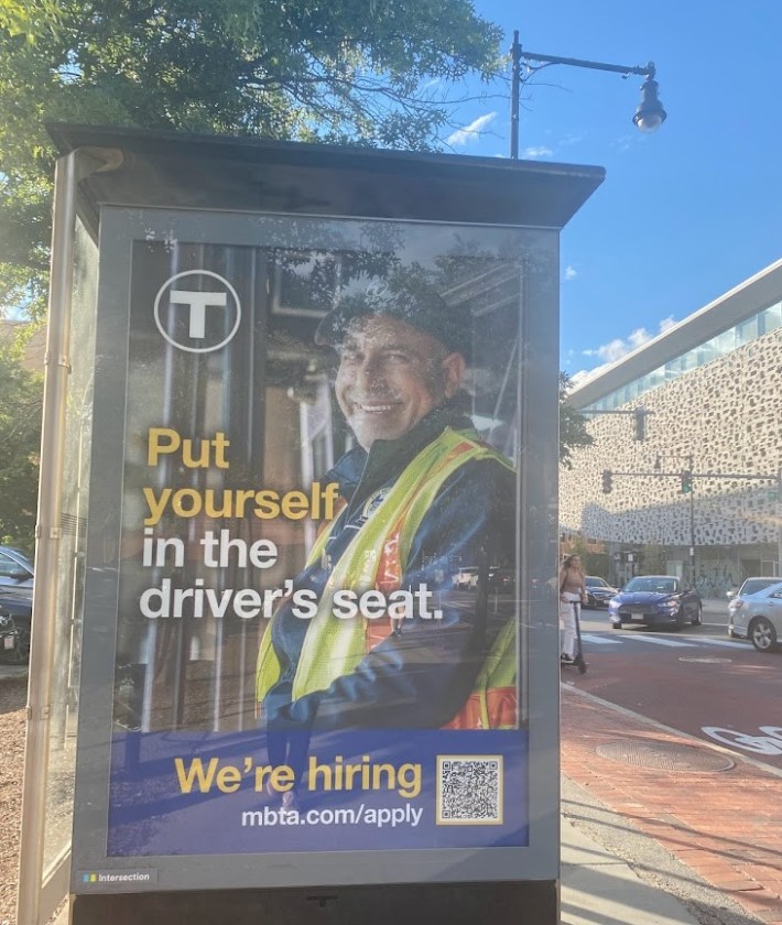 An MBTA advertisement for bus operators at a bus stop near Albany Street and Massachusetts Avenue.