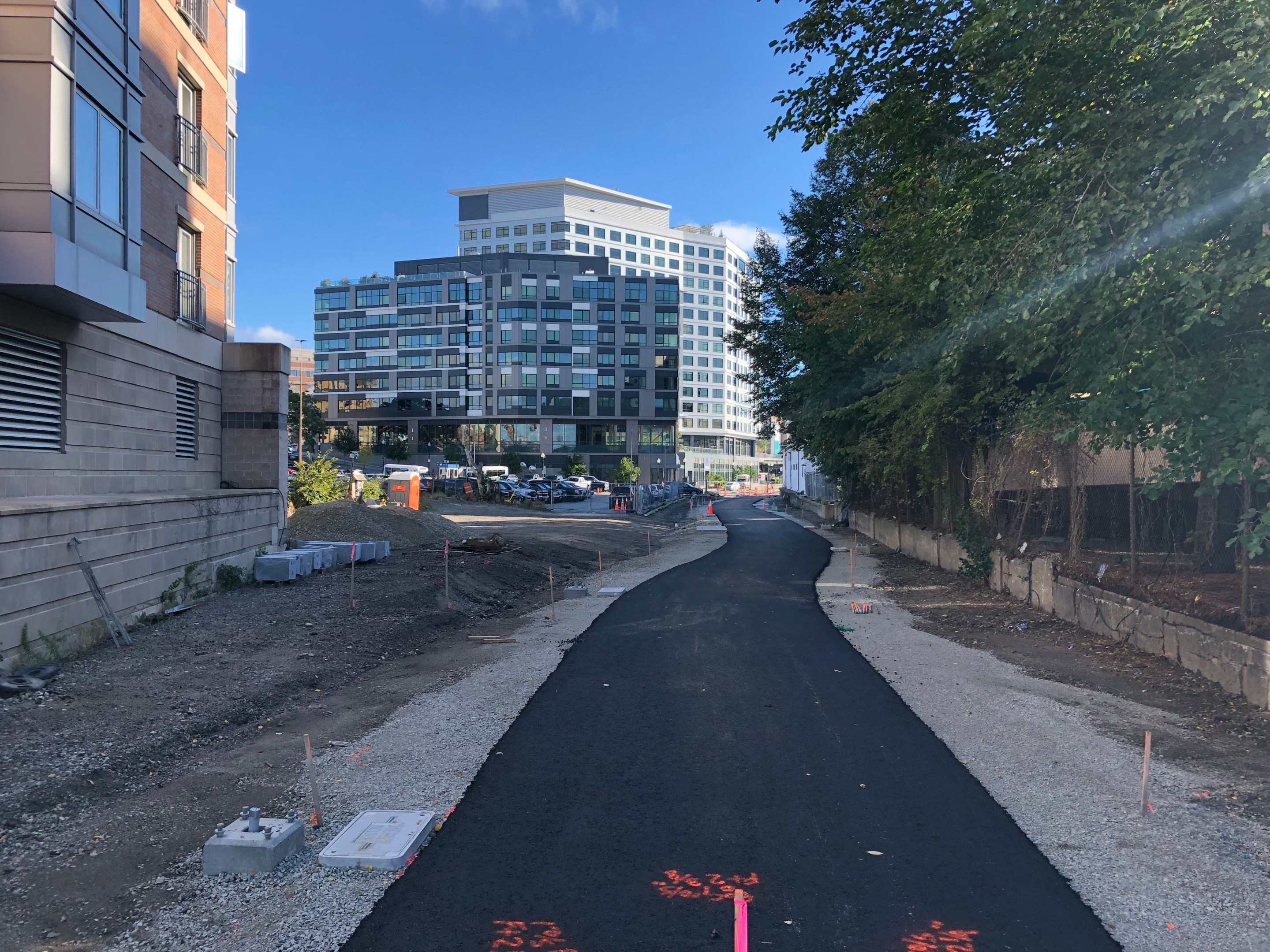 Fresh pavement on an under-construction bike path. In the distance are two new tall buildings near Kenmore Square.