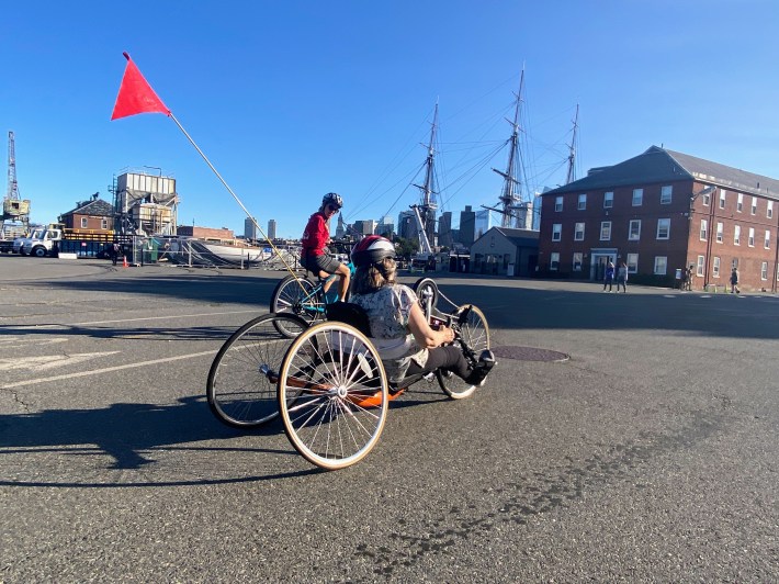 Pam Daly rides an orange recumbent bike using her hands.