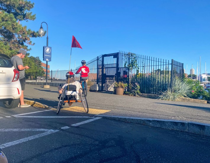 Pam Daly rides an orange recumbent bike with two wheels in the back and one in the front. she's riding onto the sidewalk from the street using a yellow ramp.