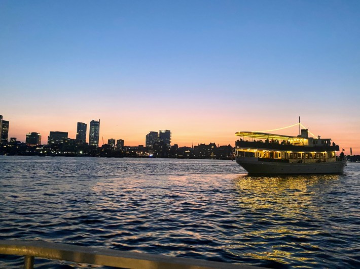 boat cruises across the harbor as twilight sets in with the Boston city skyline in the background
