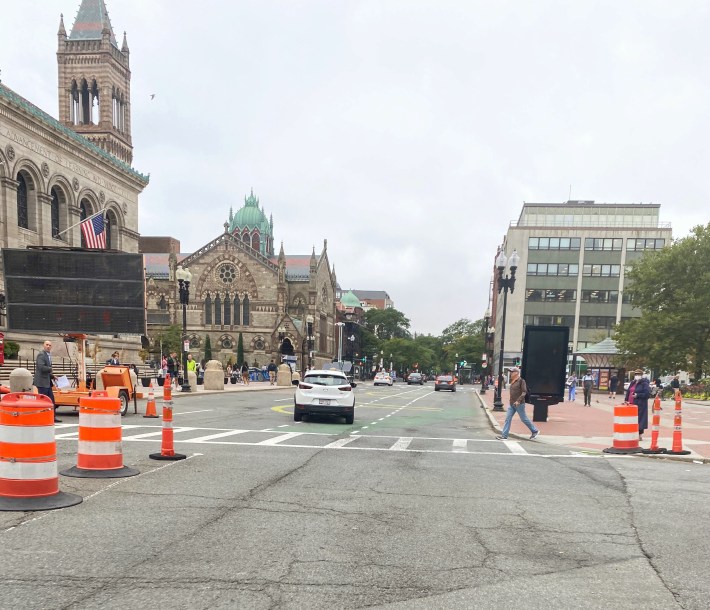 white car drives down street next to Boston Public Library