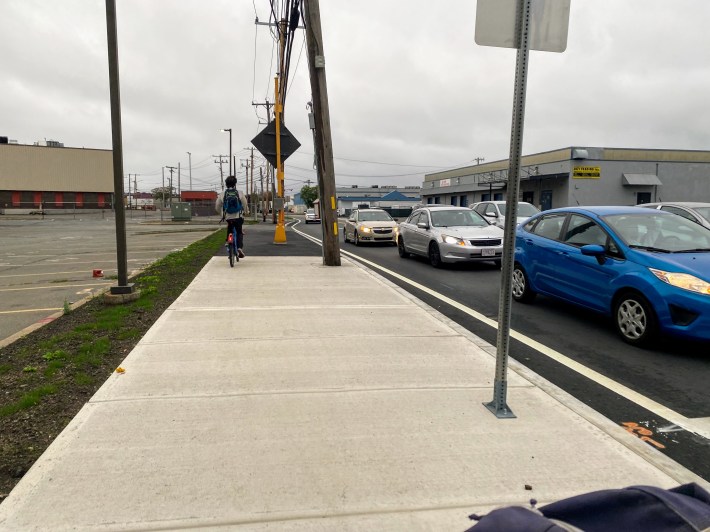 bicyclist rides on a new sidewalk in between a stretch of grass and oncoming traffic