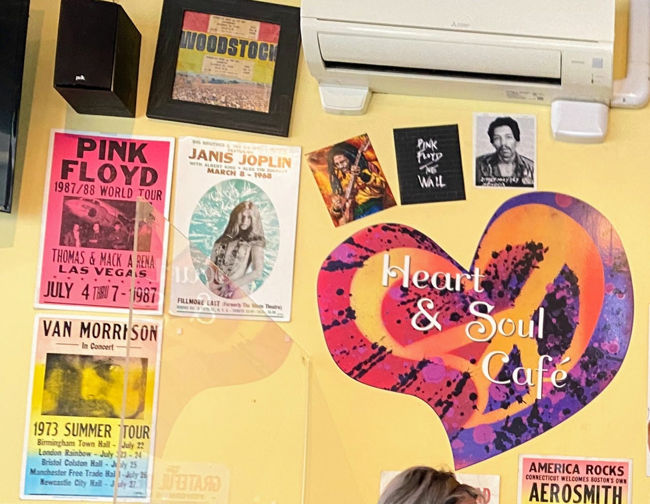 a yellow wall with differently colored posters hanging, including a heat shaped sticker reading, "Heat and Soul Cafe."