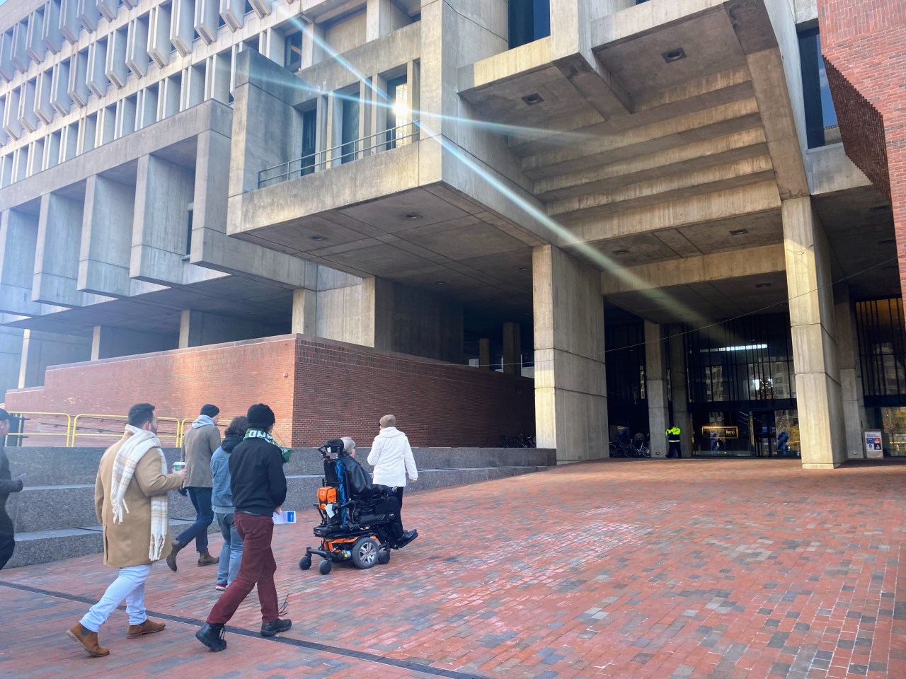 a group of people are led on a tour up the brick ramp to the main entrance of Boston City Hall.