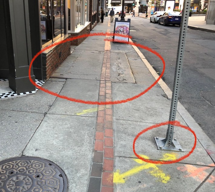 A sidewalk on School Street in Boston with a row of red bricks running down the middle to indicate the path of the Freedom Trail. Two hand-drawn circles annotate the telltale signs of an "areaway," or a hollow sidewalk, described further in the caption.