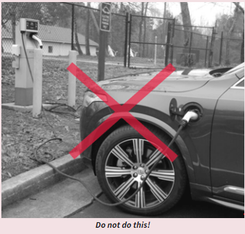 a black and white photo of an electric car charging at a station propped up on a curb without an access ramp.