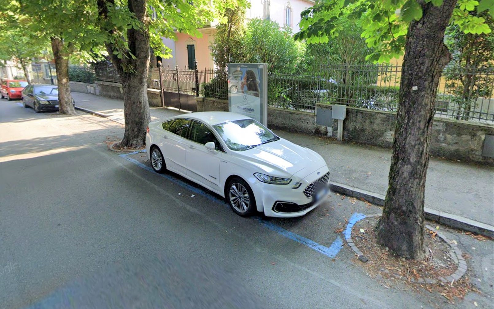 a white car is parked in between two trees planted in the street.