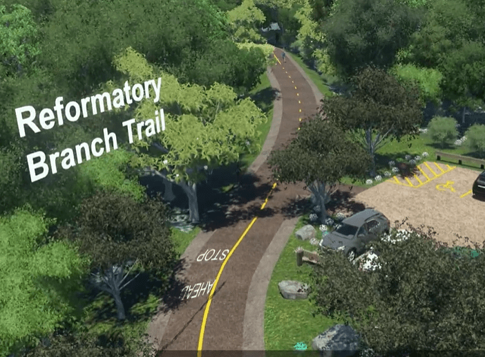 a paved bike and pedestrian path surrounded by trees next to a parking lot.