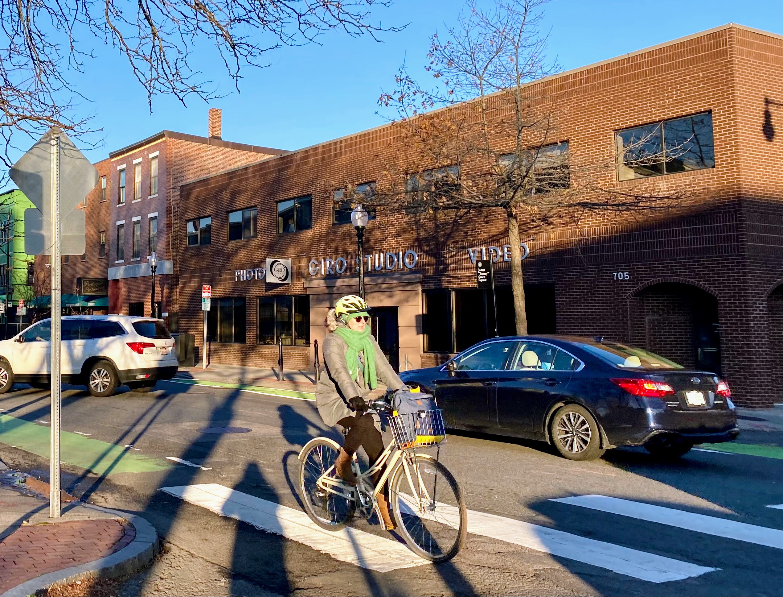 A bicyclist wearing a green scarf and a gray coat bikes down a bike lane next to cars.